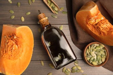 Photo of Glass bottle of oil with cut pumpkin and seeds on wooden table, flat lay