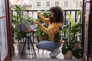 Photo of Beautiful young woman spraying potted houseplants with water on balcony