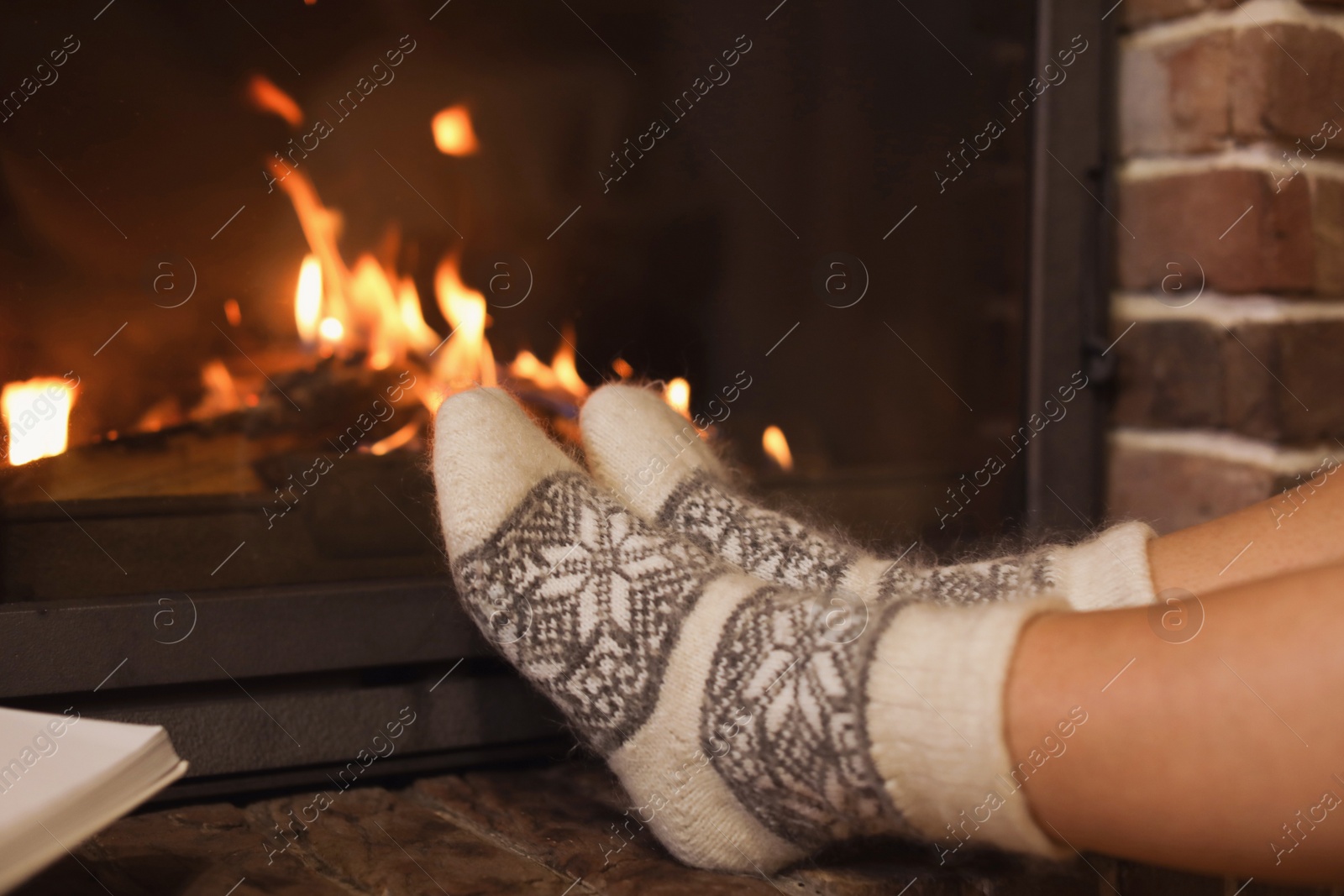 Photo of Woman in knitted socks resting near fireplace at home, closeup. Winter vacation