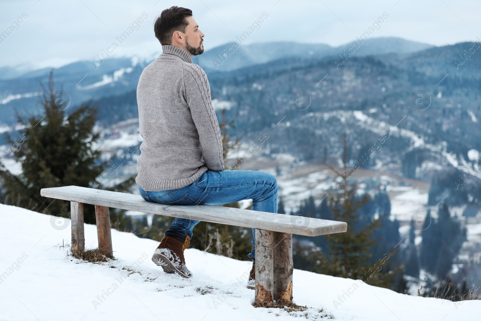 Photo of Man sitting on bench and enjoying mountain landscape, space for text. Winter vacation