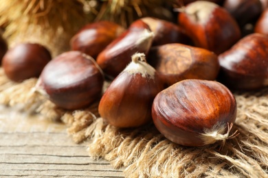 Photo of Fresh sweet edible chestnuts on wooden table, closeup