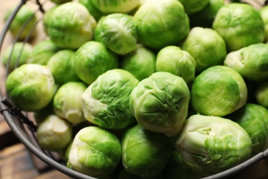 Photo of Fresh Brussels sprouts in metal basket, closeup