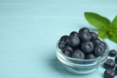 Glass bowl of tasty blueberries on color wooden table, space for text