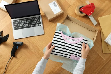 Photo of Woman packing clothes into cardboard box at wooden table, top view. Online store
