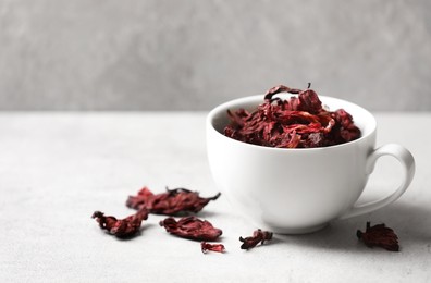 Photo of Aromatic hibiscus tea. Dried roselle calyces in cup on light table, space for text