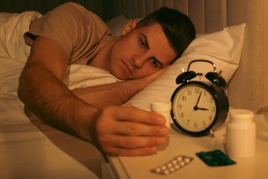 Photo of Man suffering from insomnia taking pill bottle in bed at night