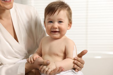 Photo of Mother applying body cream onto baby`s skin indoors, closeup