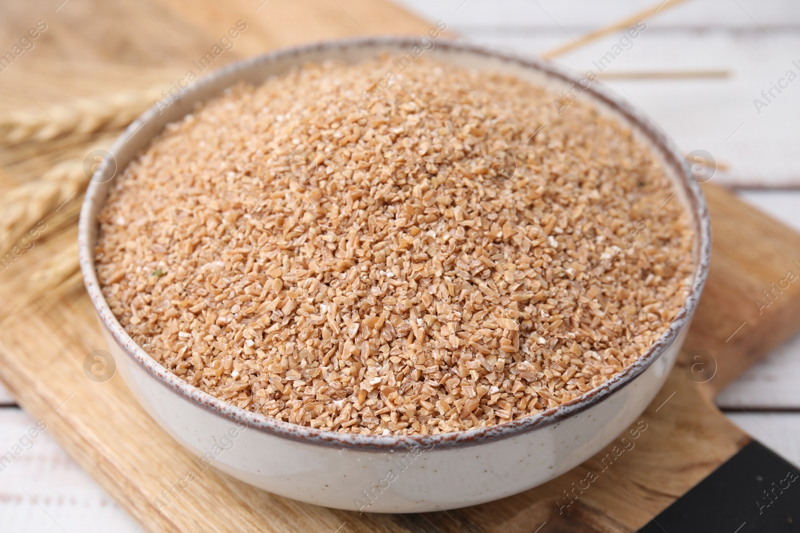 Photo of Dry wheat groats in bowl on table, closeup