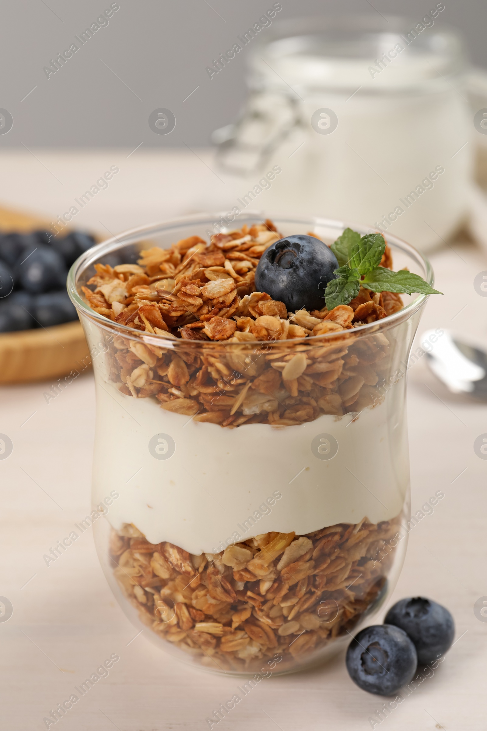 Photo of Glass of tasty yogurt with muesli and blueberries served on white wooden table