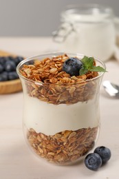 Glass of tasty yogurt with muesli and blueberries served on white wooden table