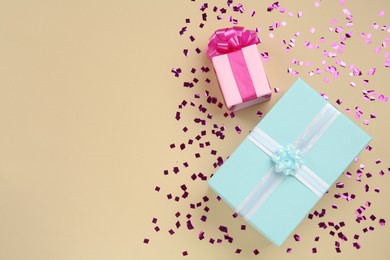 Gift boxes and shiny confetti on beige background, flat lay. Space for text