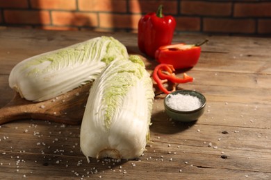 Fresh Chinese cabbages, bell peppers and salt on wooden table