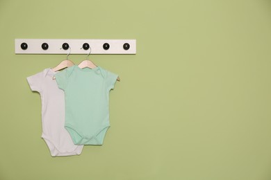Baby onesies hanging on green wall, space for text. Interior design