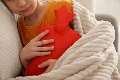 Photo of Ill boy with hot water bottle suffering from cold at home, closeup