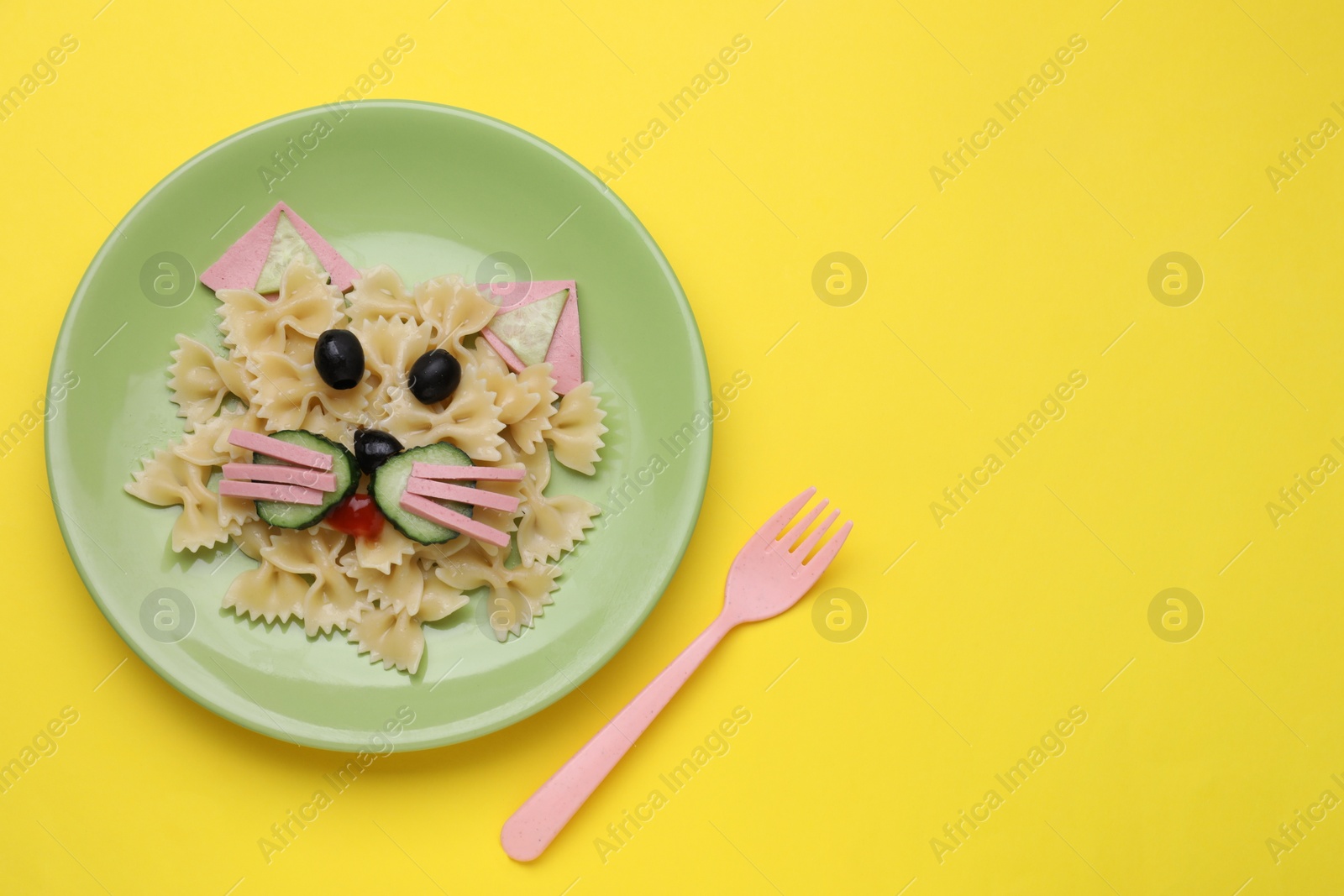 Photo of Creative serving for kids. Plate with cute cat made of tasty pasta, vegetables and sausage on yellow background, flat lay. Space for text