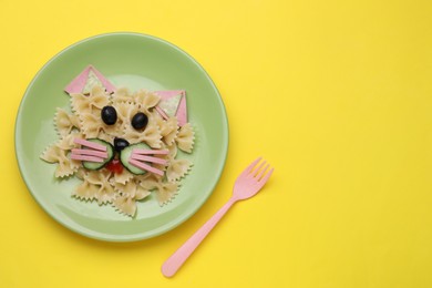 Photo of Creative serving for kids. Plate with cute cat made of tasty pasta, vegetables and sausage on yellow background, flat lay. Space for text