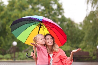 Happy mother and daughter with bright umbrella under rain outdoors