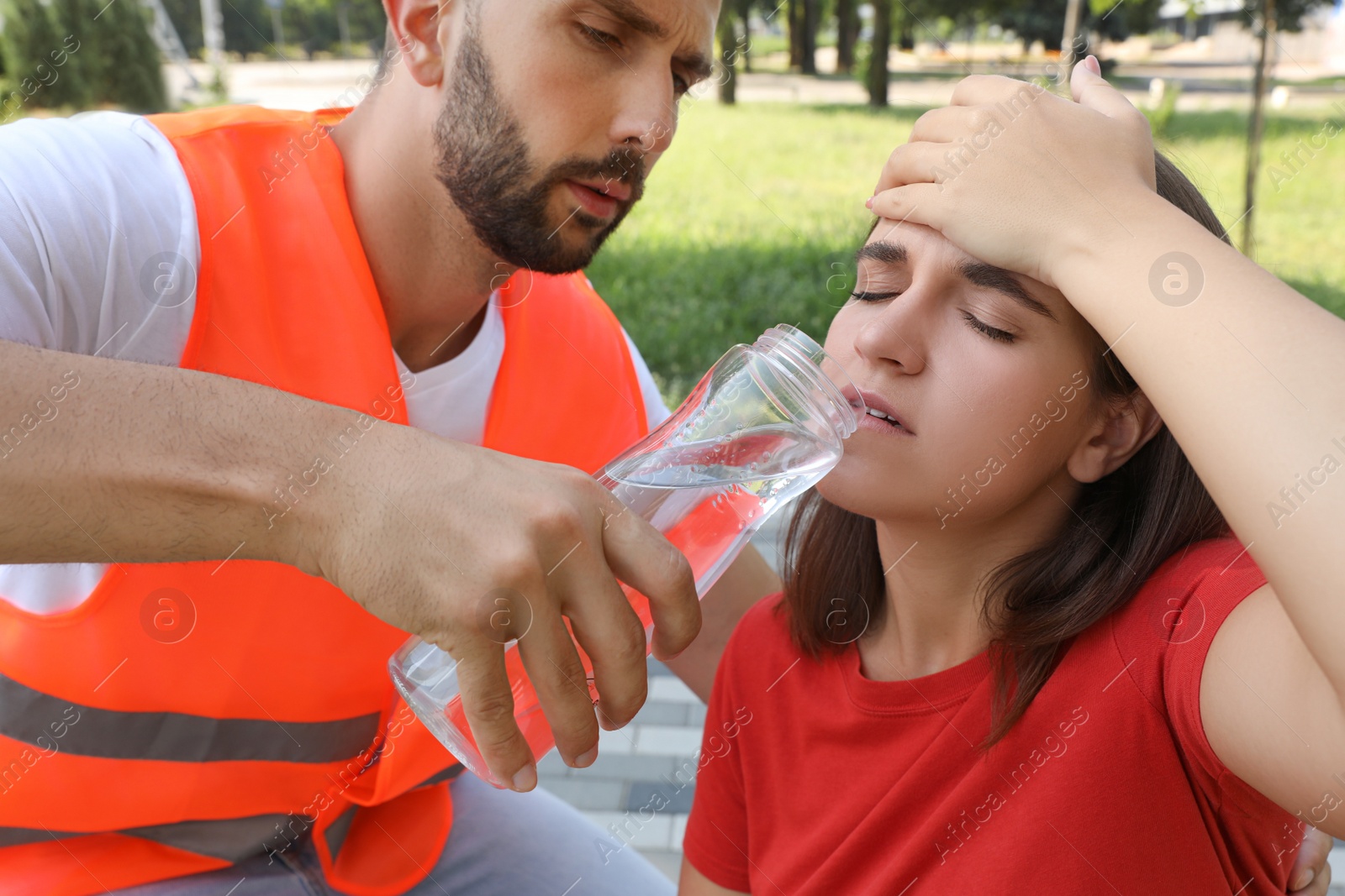 Photo of Worker with bottle of water helping woman outdoors. Suffering from heat stroke