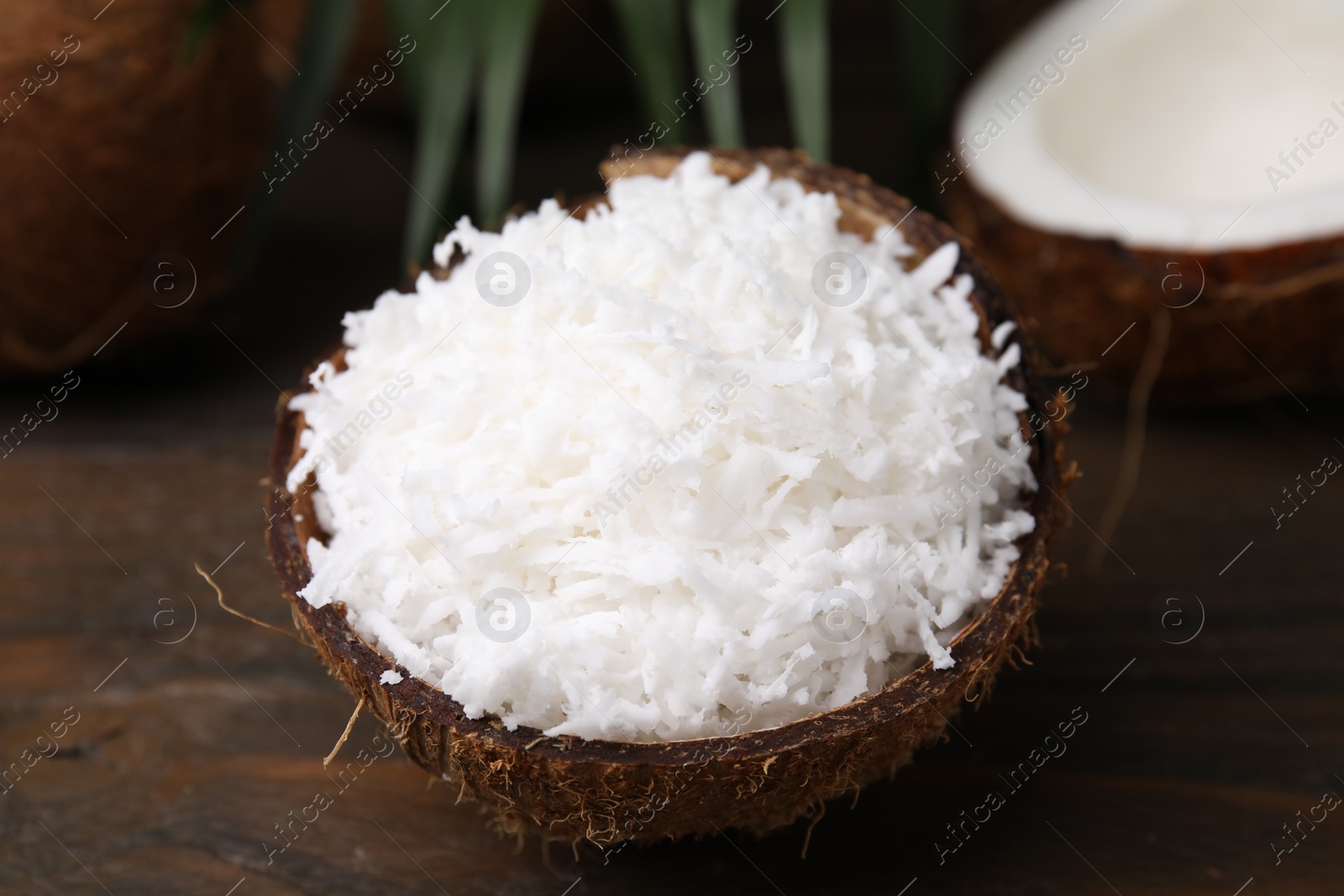 Photo of Coconut flakes in nut shell on wooden table, closeup