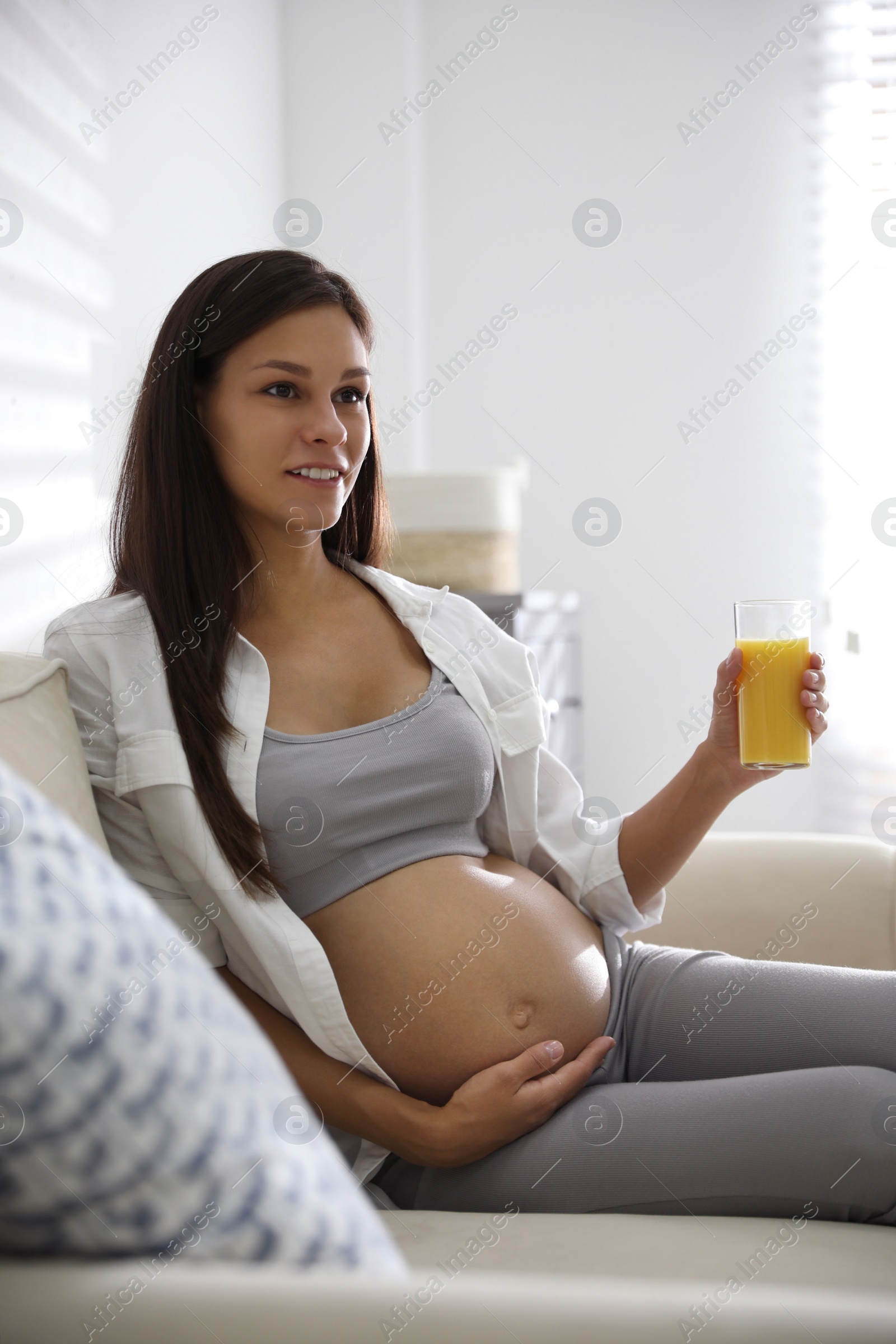 Photo of Young pregnant woman with glass of juice in living room. Taking care of baby health