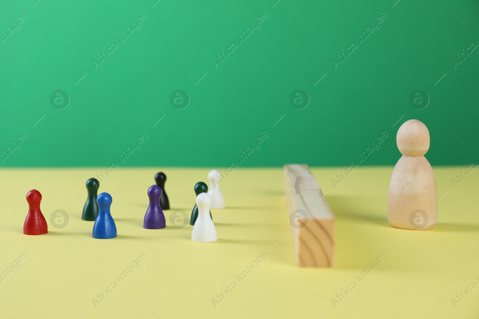 Photo of Barriers and difficulties in communication. Wooden blocks separating small human figures from one big on yellow surface, space for text
