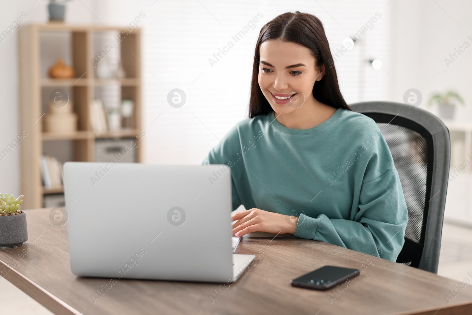 Photo of Young woman watching webinar at table in room