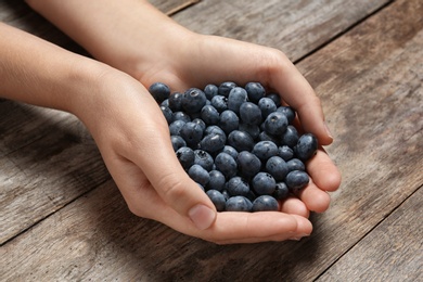 Photo of Woman holding juicy fresh blueberries on wooden table
