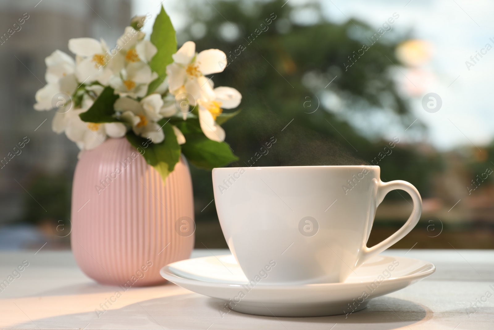 Photo of Cup of delicious morning coffee and vase with flowers on table outdoors