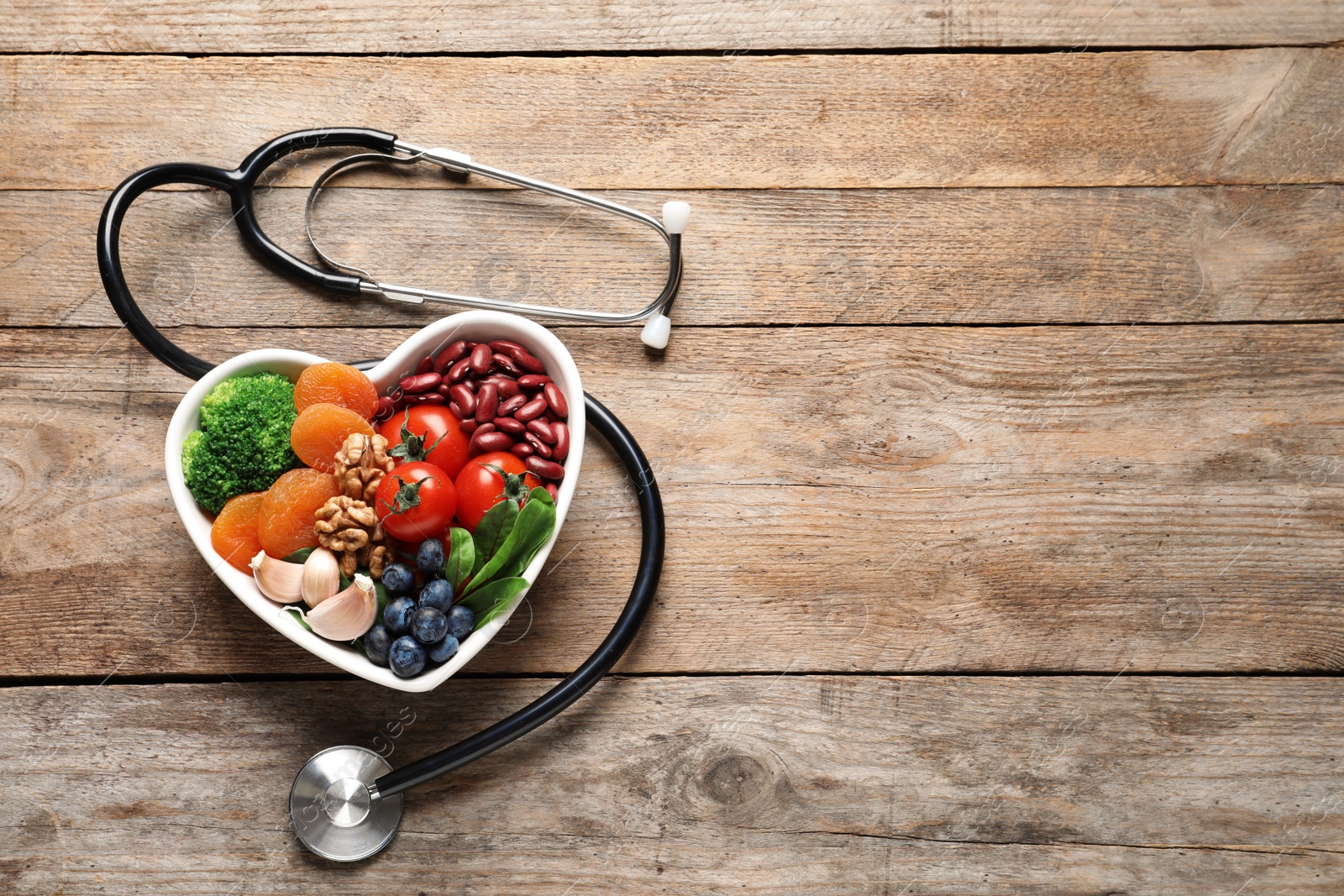 Photo of Bowl with heart-healthy diet products and stethoscope on wooden background, top view. Space for text