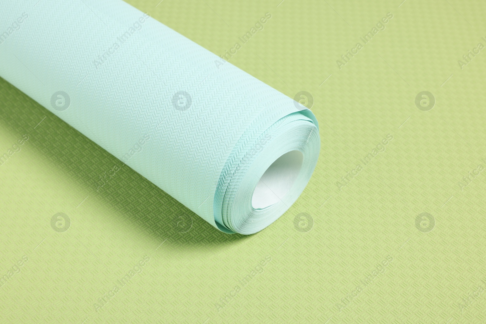 Photo of One light turquoise wallpaper roll on green sample, space for text