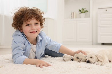 Little boy lying with cute puppies on white carpet at home
