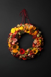 Photo of Beautiful autumnal wreath with flowers, berries and fruits hanging on black background. Space for text