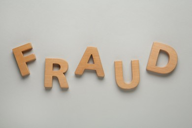 Photo of Word Fraud made of wooden letters on grey background, flat lay