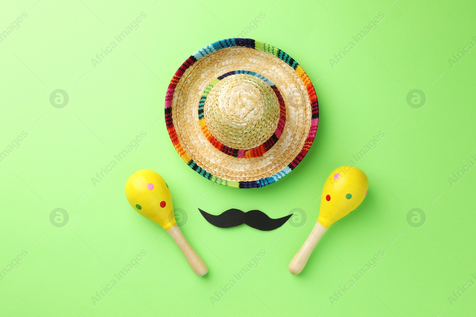 Photo of Mexican sombrero hat, fake mustache and maracas on green background, flat lay