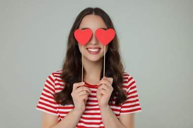 Photo of Young woman covering her eyes with paper hearts on grey background
