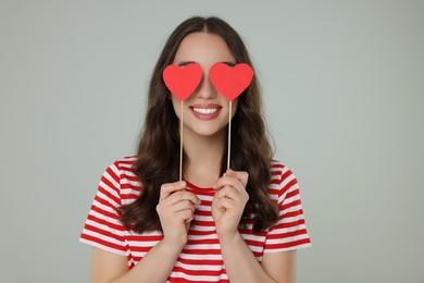 Young woman covering her eyes with paper hearts on grey background