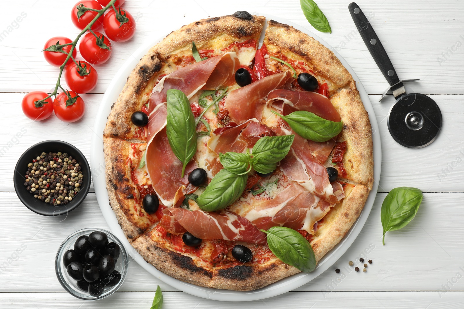 Photo of Tasty pizza with cured ham, olives, tomatoes and basil on white wooden table, flat lay