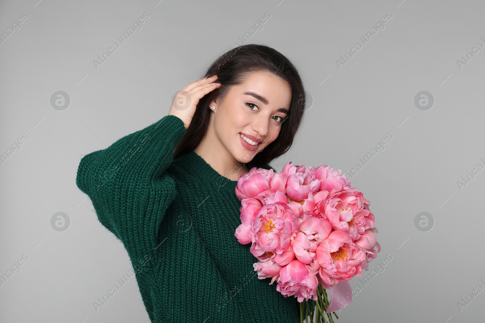 Photo of Beautiful young woman with bouquet of peonies on light grey background