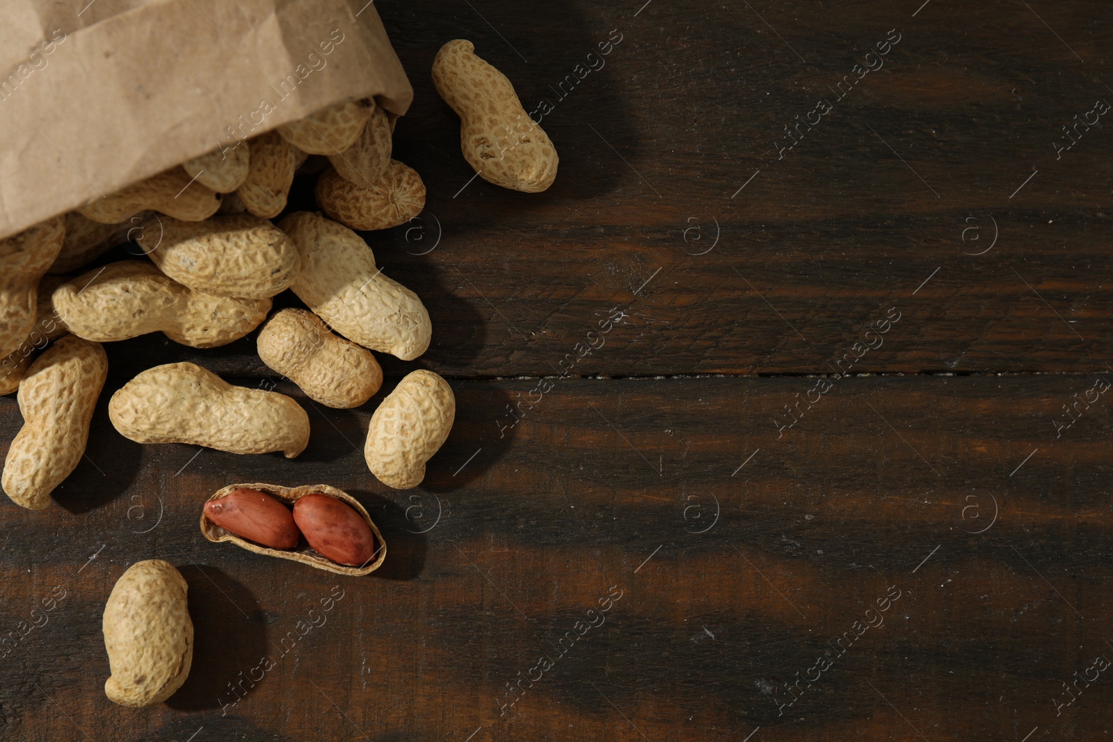 Photo of Paper bag with fresh unpeeled peanuts on wooden table, top view. Space for text