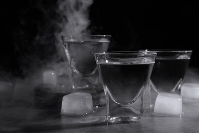 Photo of Vodka in shot glasses with ice on table against black background