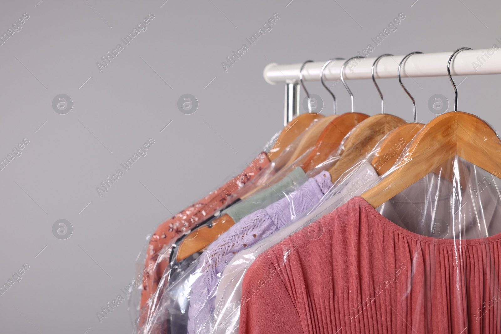 Photo of Dry-cleaning service. Many different clothes in plastic bags hanging on rack against grey background, space for text