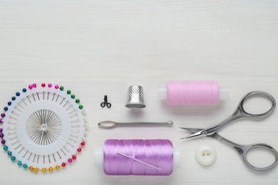 Flat lay composition with thimble and different sewing tools on white wooden table. Space for text