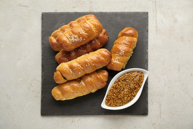 Photo of Delicious sausage rolls and grain mustard on beige table, top view