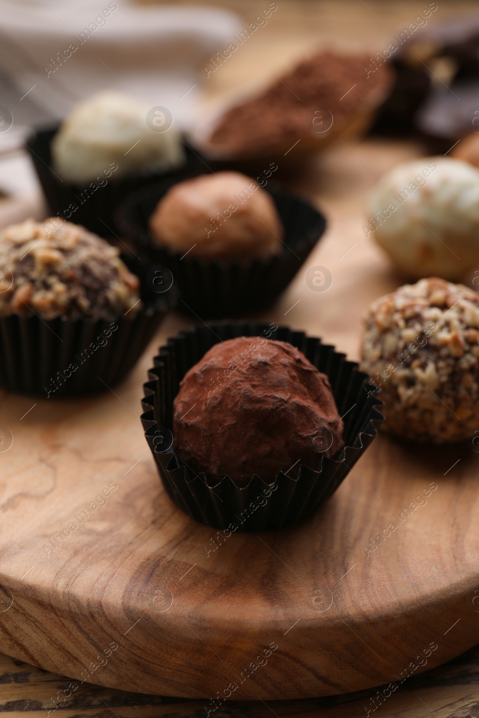 Photo of Different tasty chocolate candies on wooden board, closeup