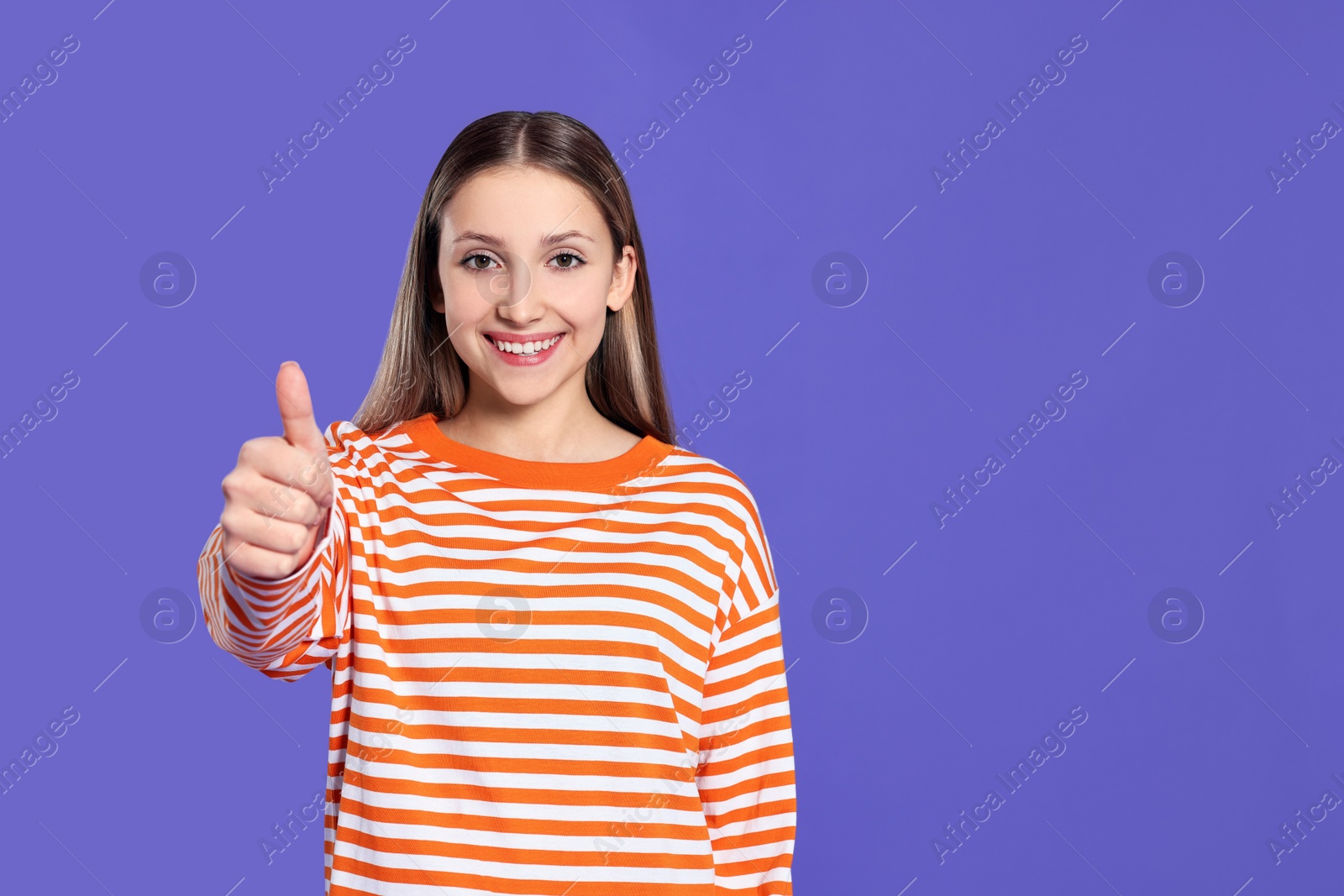 Photo of Beautiful teenage girl showing thumb up on purple background. Space for text
