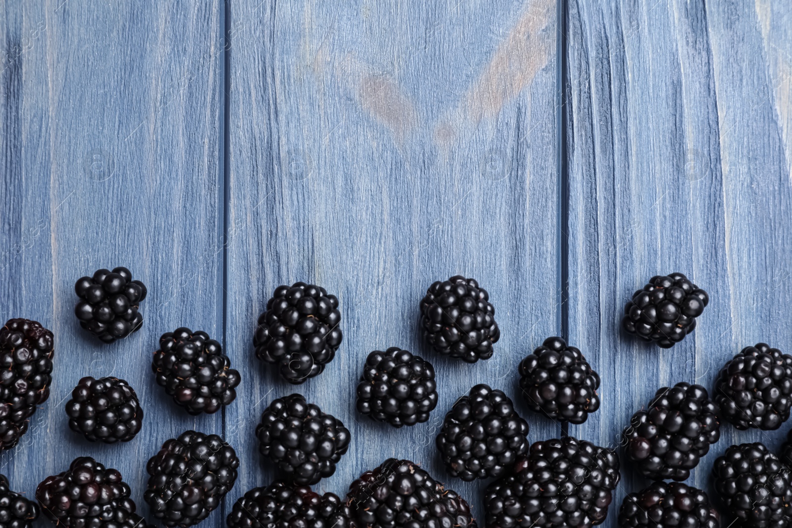 Photo of Fresh ripe blackberries on blue wooden table, flat lay. Space for text