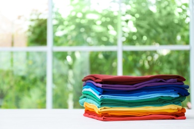 Stack of bright folded clothes on table against blurred background. Space for text