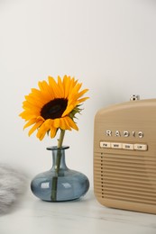 Vase with beautiful sunflower and radio on white marble table