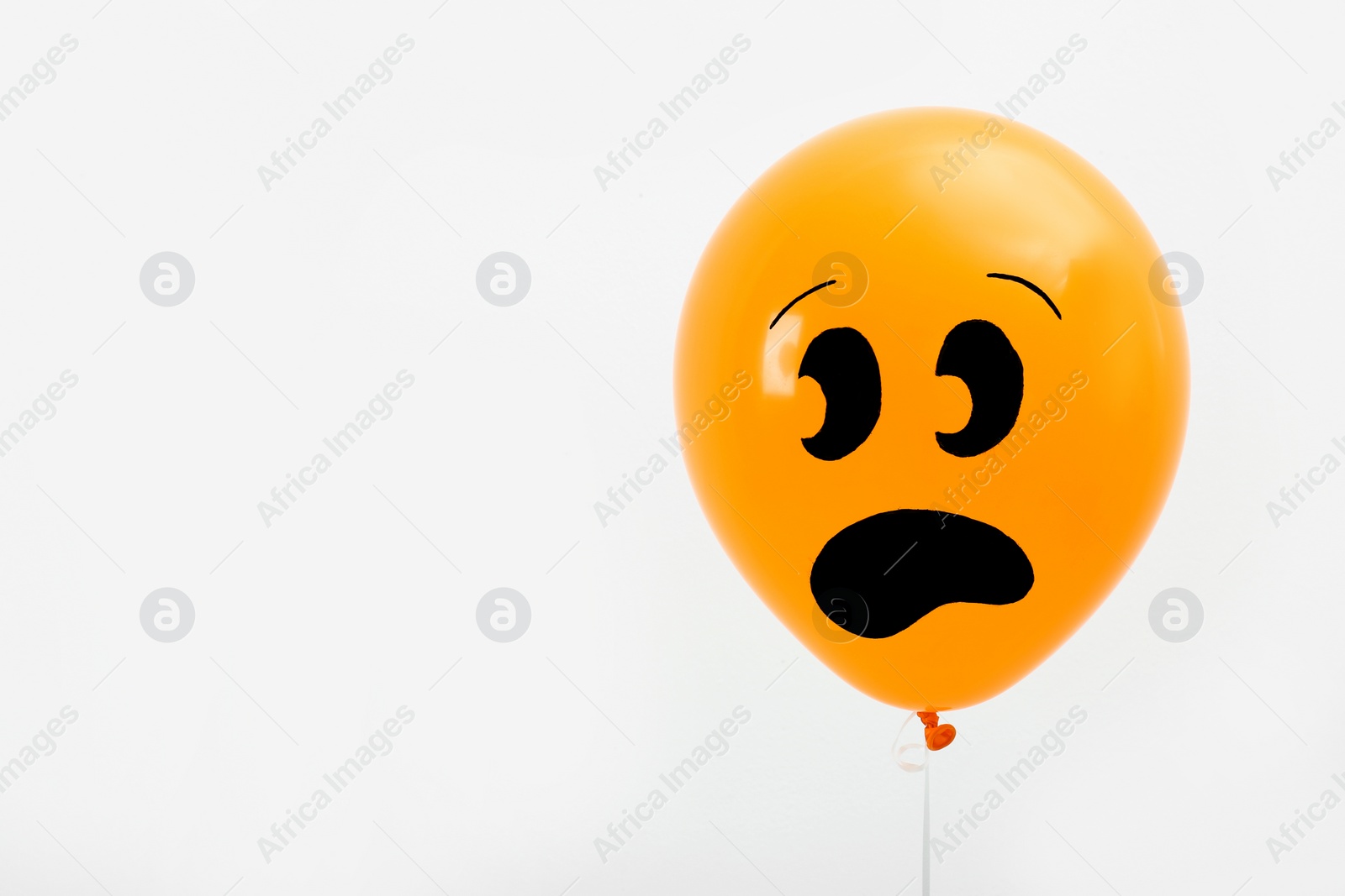 Photo of Orange balloon with drawing of scared face on light background, space for text. Halloween party