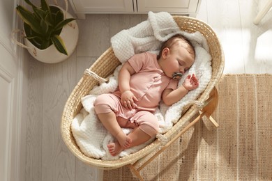 Photo of Cute little baby with pacifier sleeping in wicker crib at home, top view